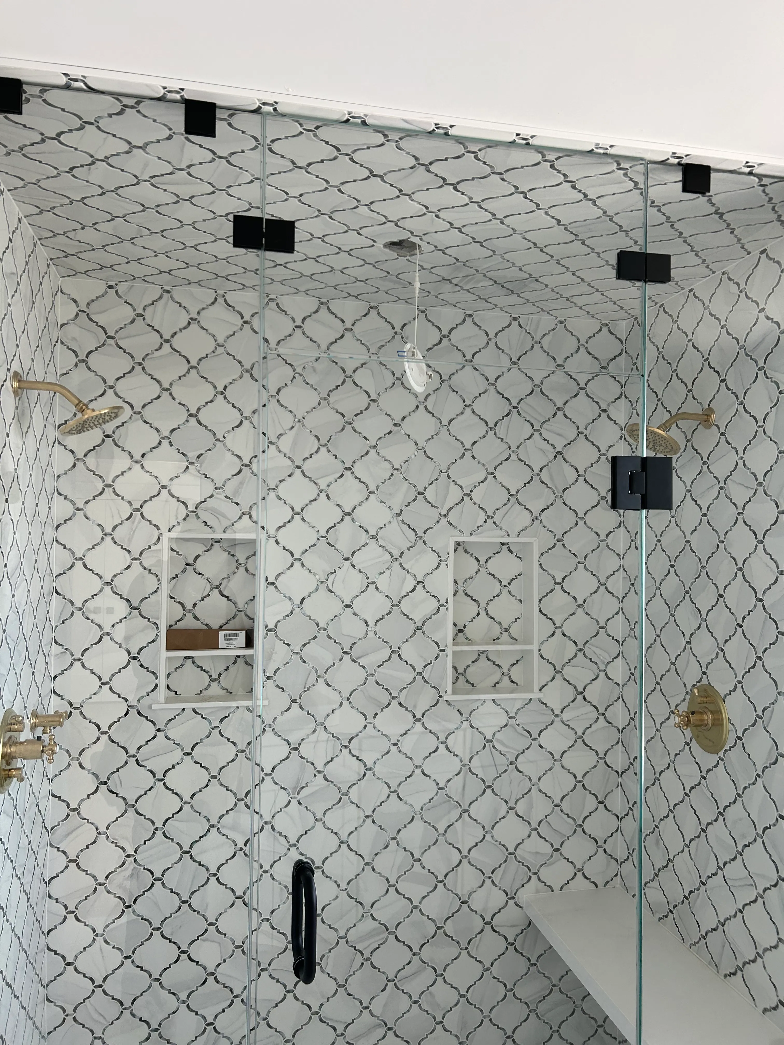Wider view of the same arabesque-tile shower with built-in niches and brass fixtures