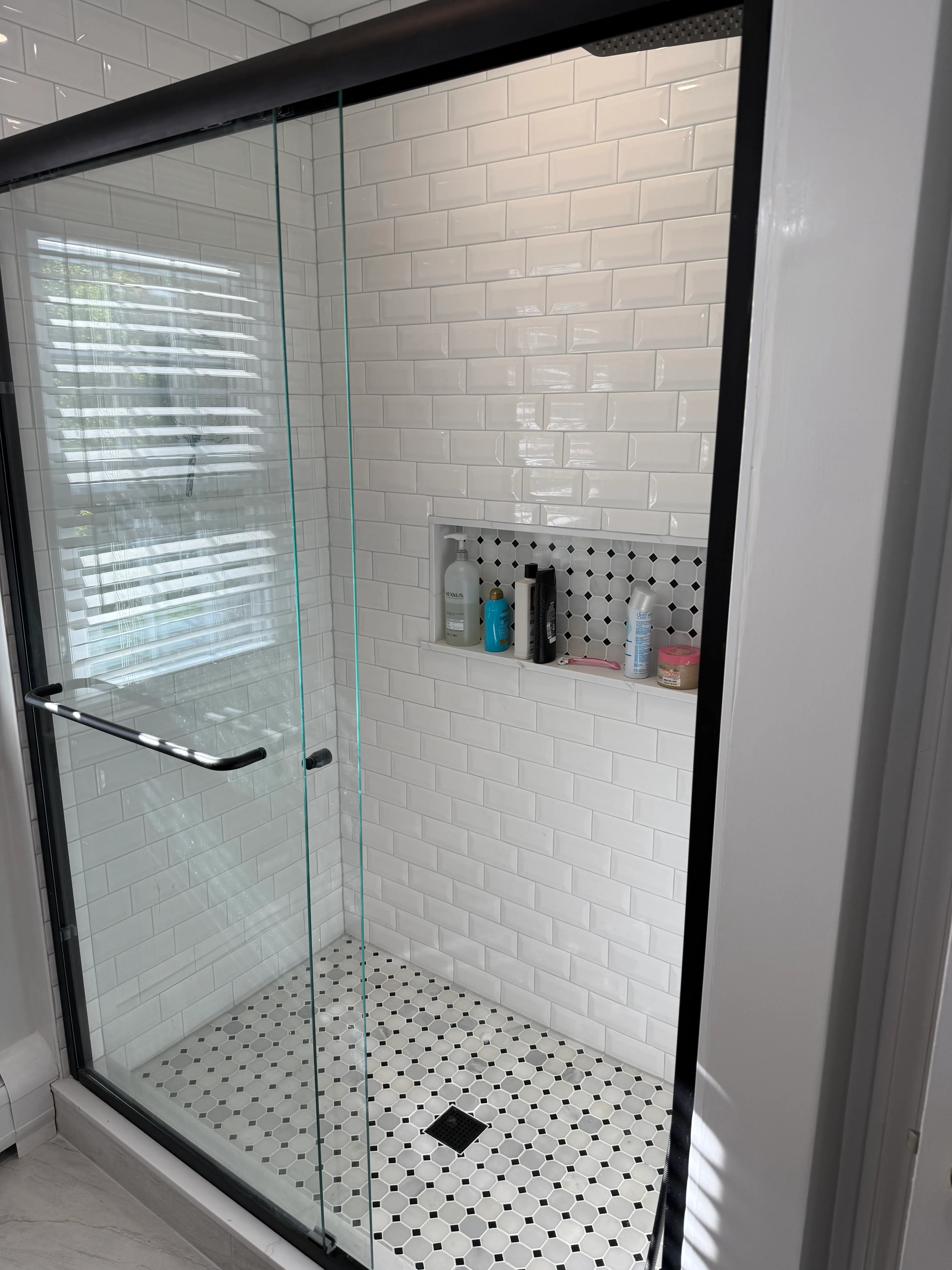 Black-framed glass shower with beveled subway tile and penny-tile floor