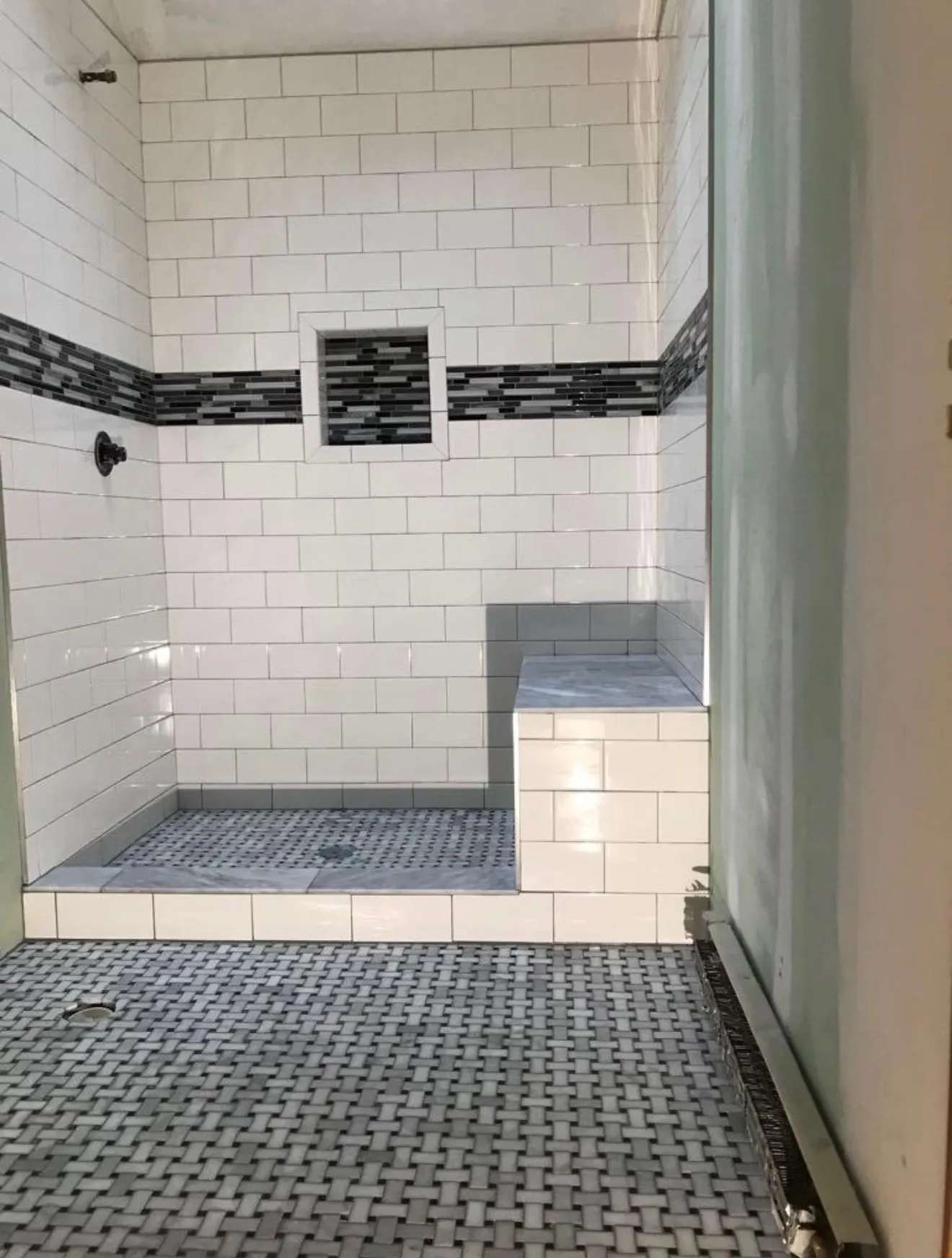 White-subway shower with glass-mosaic accent strip, built-in niche, and basket-weave mosaic floor
